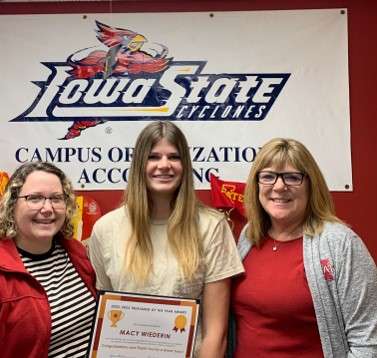 A group of three women, with the 2022-2023 winner Macy Wiederin in the middle holding a certificate for the Treasurer of the Year Award. .